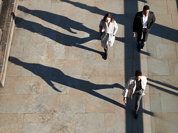 Three office workers walking down an urban street, casting shadows